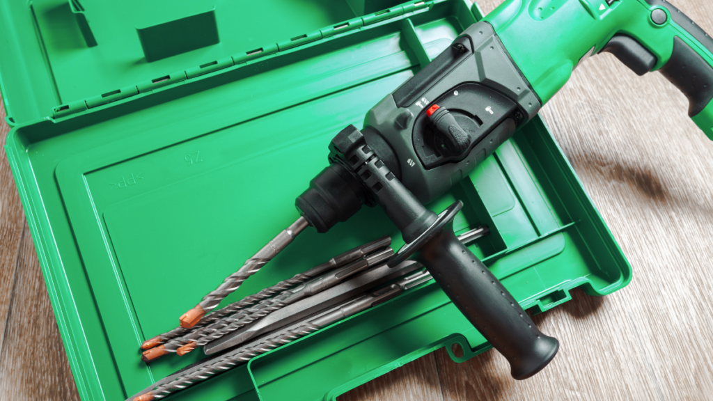 Martelete perfurador verde com empunhadura lateral e brocas para concreto dentro de maleta plástica, sobre superfície de madeira. Termos de uso